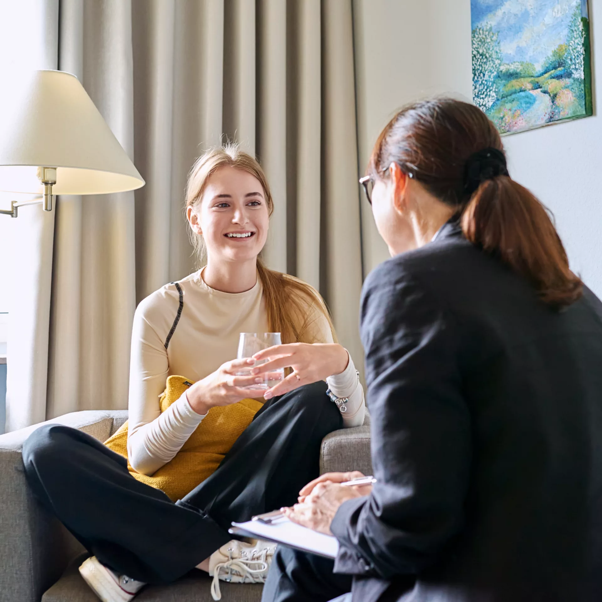 Young female teenager talking with counselor, teacher sitting in chair in office